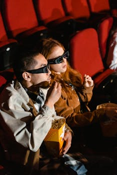 Man and woman wearing 3D glasses enjoying popcorn in a movie theater.