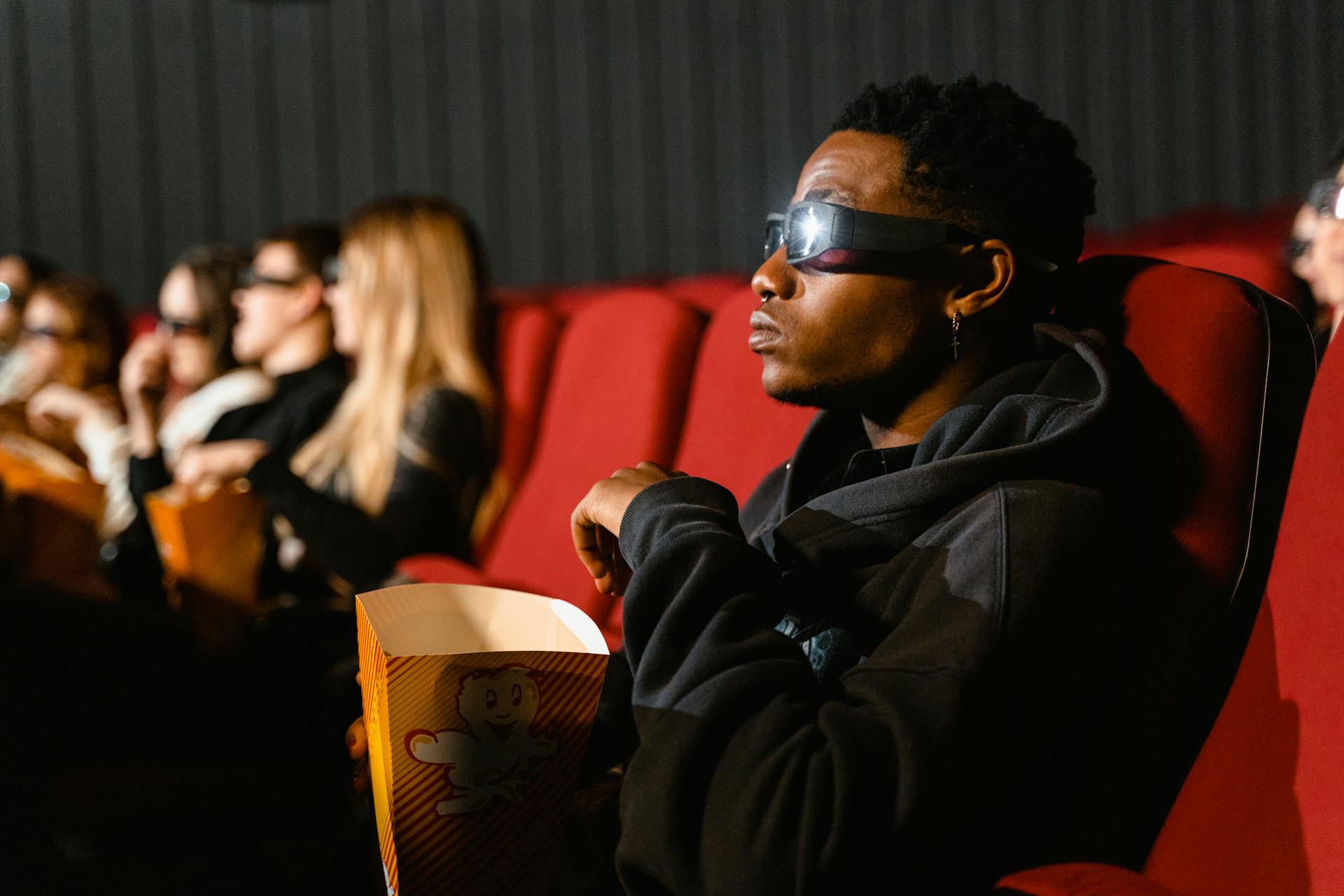 A Man in Black Hoodie Sweater Wearing a Black Eyewear Holding a Bucket of Popcorn