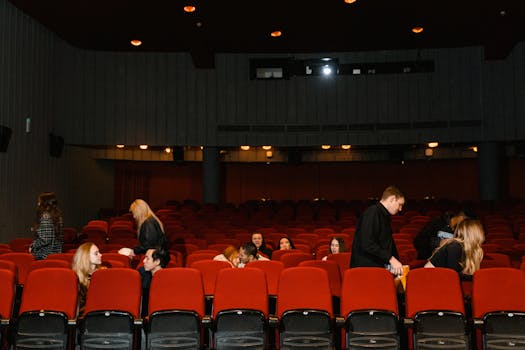 A diverse group of adults inside a theater with red seats and soft lighting.