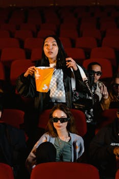 People in 3D glasses eating popcorn during a movie in a theater.