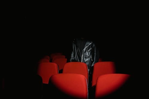 Person in Black Leather Jacket Standing Behind Red Theater Seat