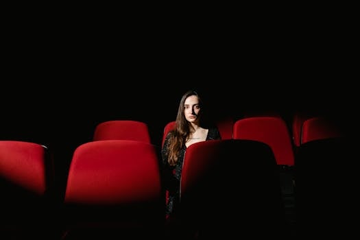 A single woman sits alone in a dimly lit cinema theater, evoking solitude and introspection.