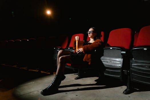 A woman sits alone in a dimly lit cinema, enjoying popcorn in an empty theater.