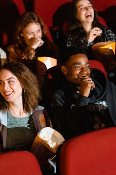 Group of diverse friends laughing and enjoying popcorn while watching a movie in a theater.