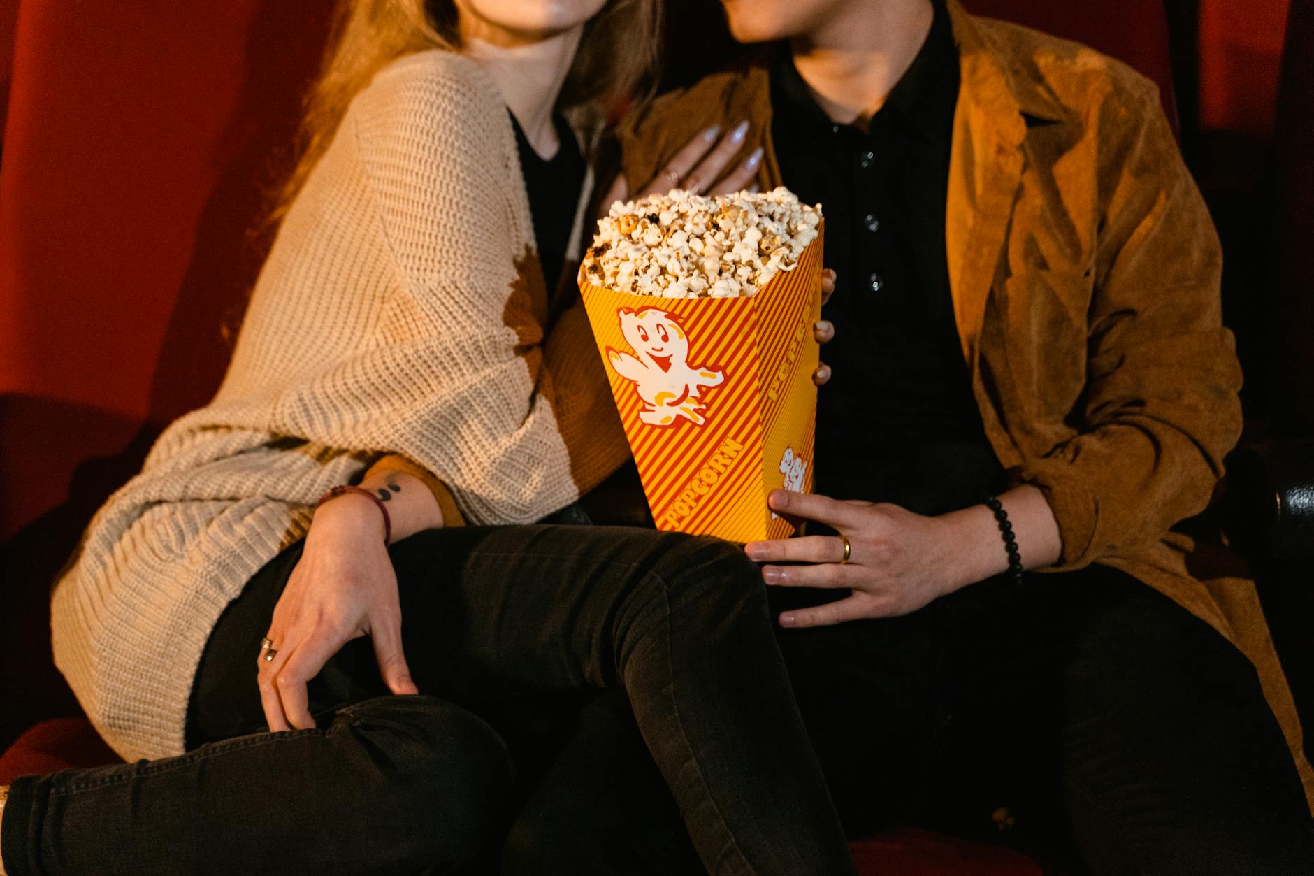 Couple seated in a cozy cinema, sharing popcorn during a movie night.