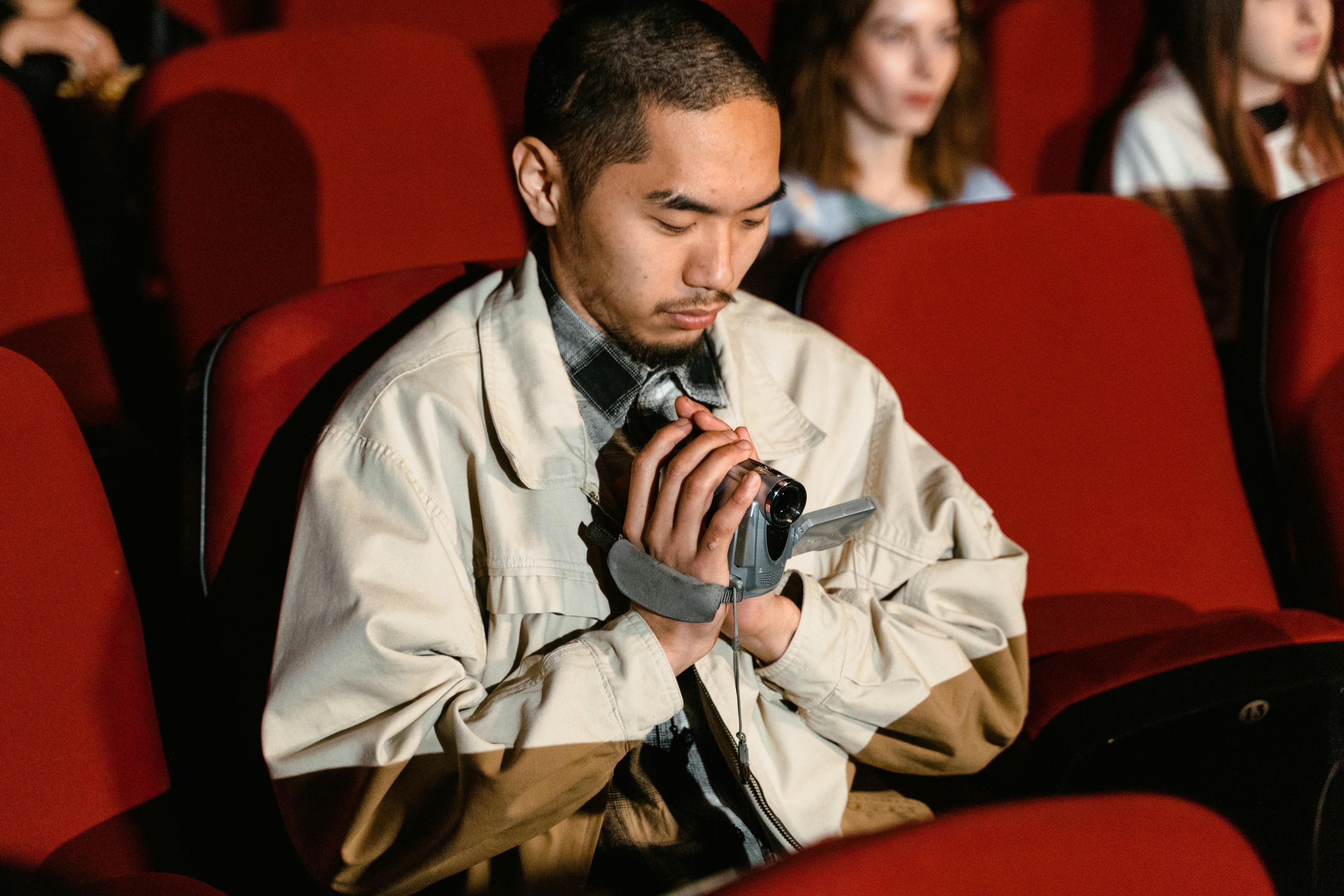 a man sitting while holding a video recorder inside the cinema