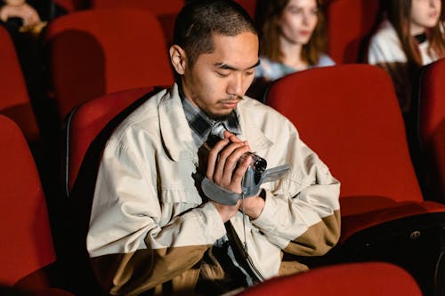 A Man Sitting while Holding a Video Recorder Inside the Cinema