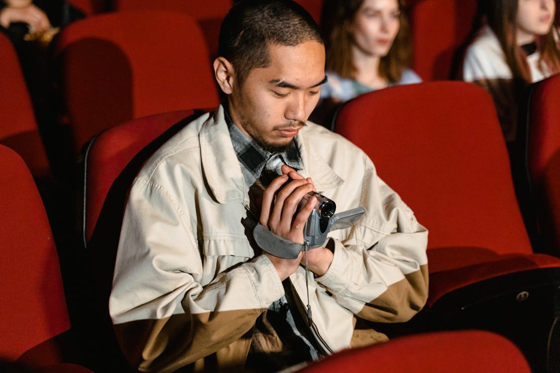 A Man Sitting while Holding a Video Recorder Inside the Cinema