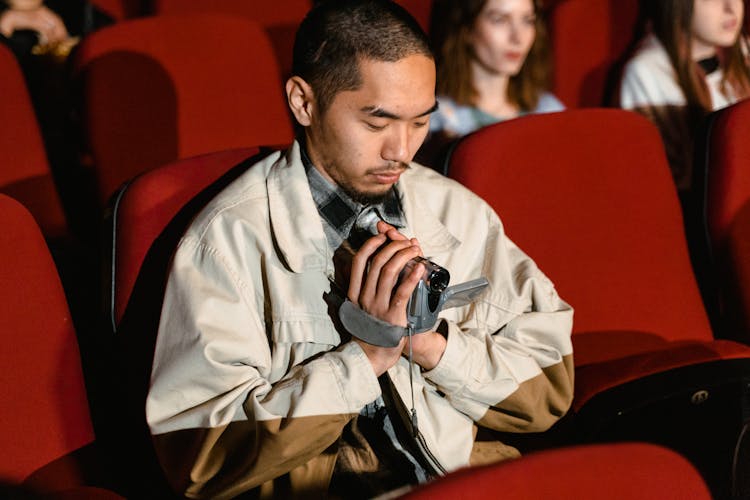 A Man Sitting While Holding A Video Recorder Inside The Cinema