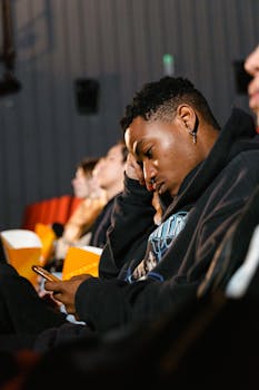 Man in a hoodie using a mobile phone in a cinema setting.