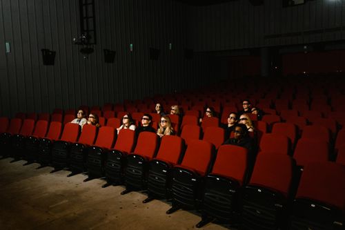Free Small group of people wearing 3D glasses watching a movie in a theater with red seats. Stock Photo