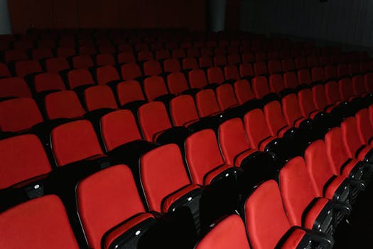 A view of empty red theater seats arranged in rows inside a cinema hall.