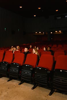 A small group of people watching a movie in a dark theater with red seats.