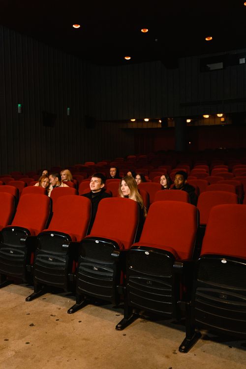 Free A small group of people watching a movie in a dark theater with red seats. Stock Photo