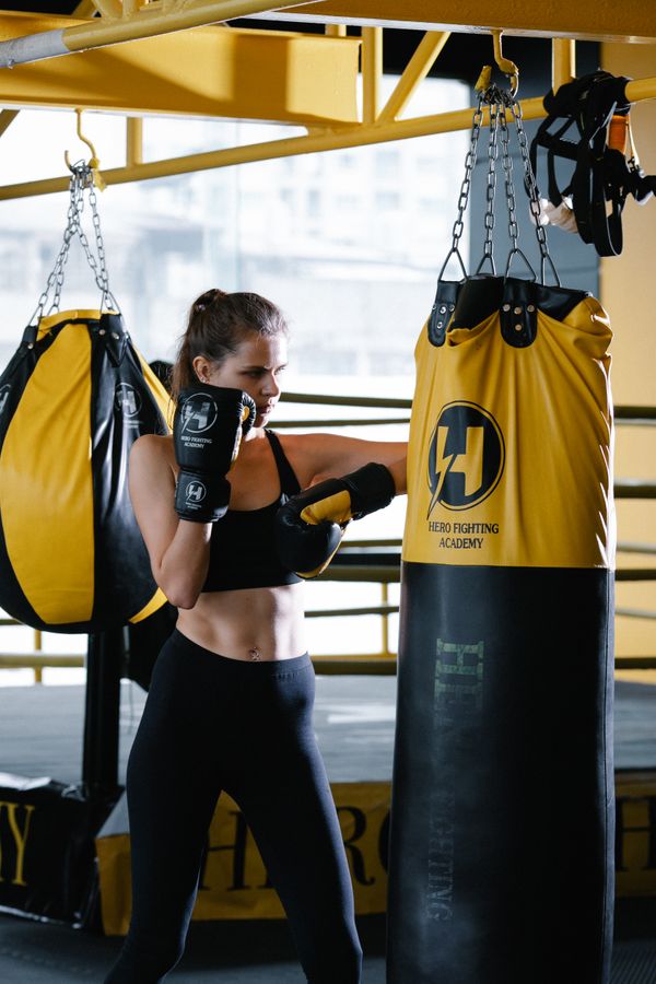 Woman in activewear with boxing gloves hitting a punching bag, representing the conditioning zone
