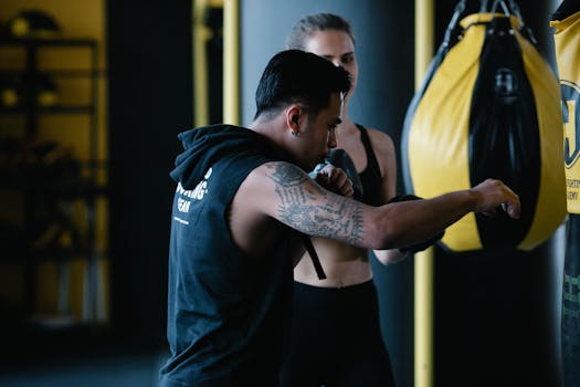 Two athletes focused on boxing training with a punching bag in an indoor gym setting.