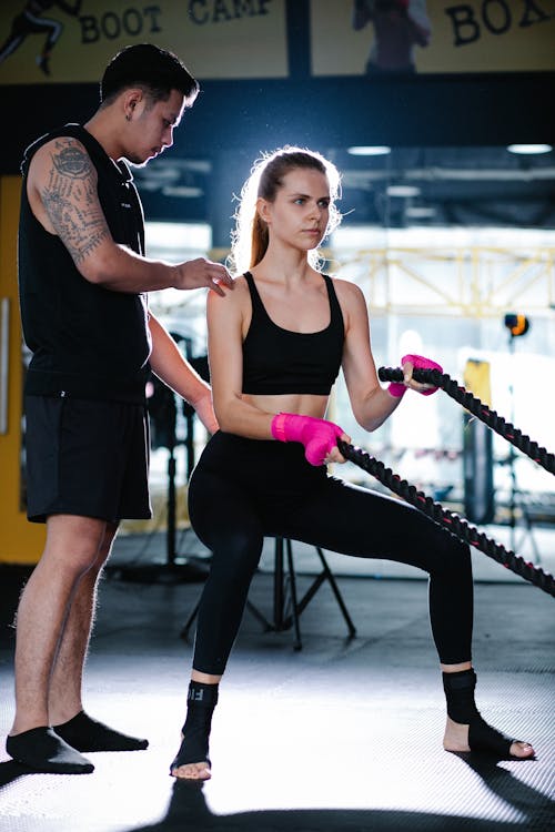 Latin American instructor helping woman exercising with battle ropes