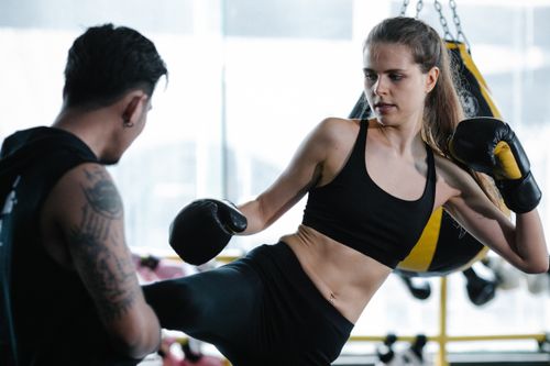 Free Anonymous personal instructor helping sportive female fighter to do kicking exercise during intense kickboxing training in gym with punching bag Stock Photo