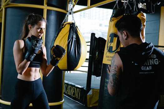 Sportive female in activewear standing in fighting stance while practicing punches with unrecognizable personal instructor during workout in modern gym