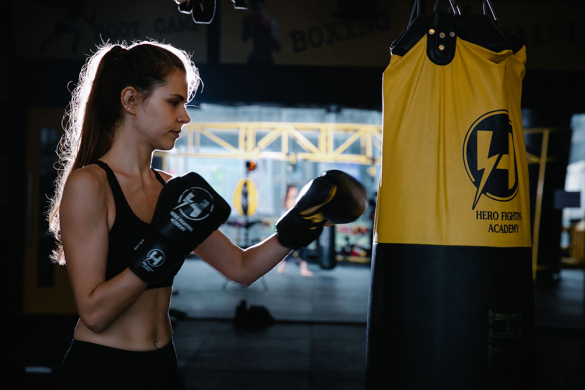 Side view of motivated young fir sportswoman with long hair in activewear and protective gloves punching bag while practicing boxing alone in modern gym