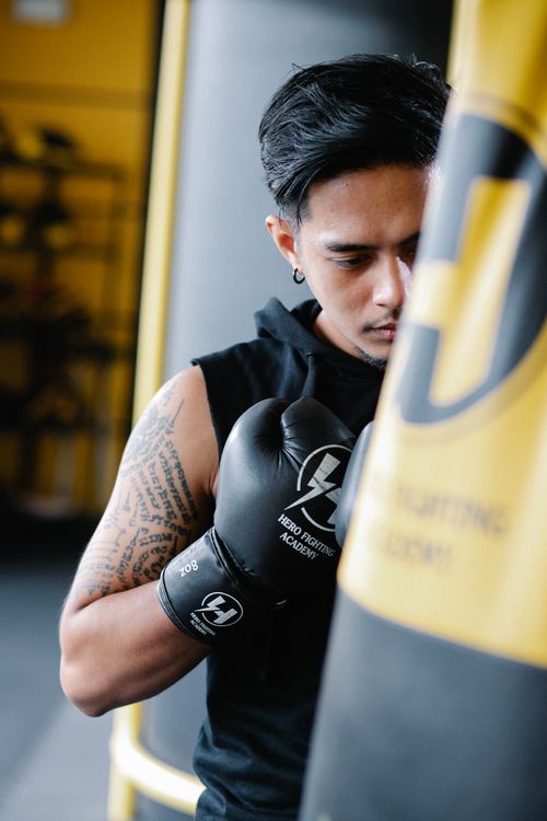 Free Strong muscular Latin American male boxer with tattoo on arm punching bag while training in light gym Stock Photo