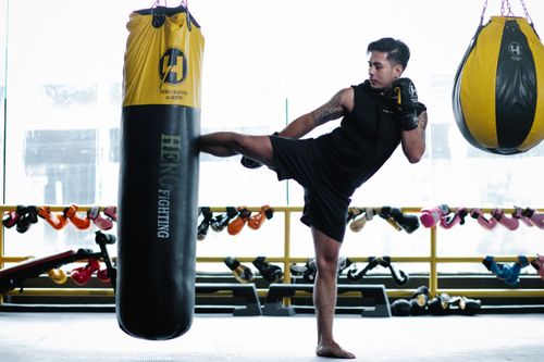 Free Side view full body of strong Asian sportsman kicking heavy punch bag during workout in gym Stock Photo