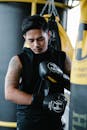 Asian man in activewear concentrating while putting on boxing gloves during training in gym