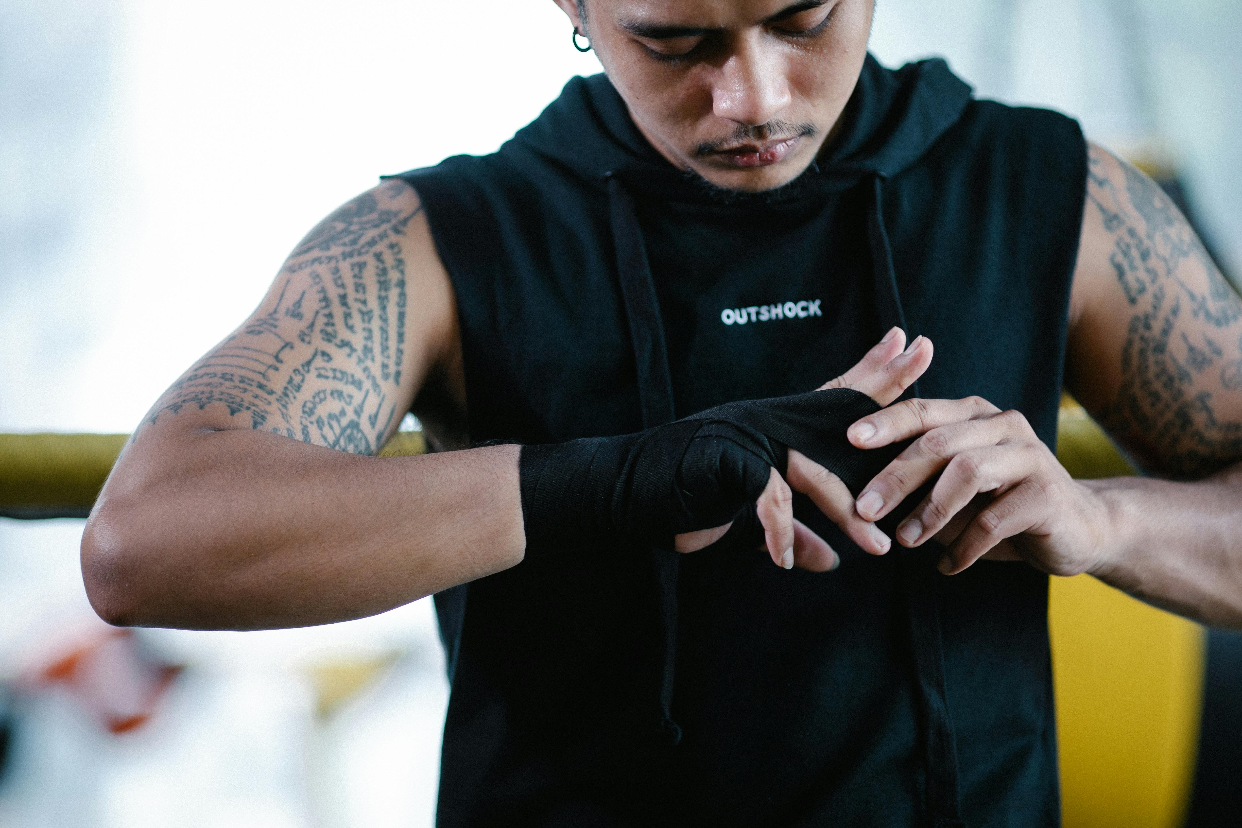 brutal ethnic boxer bandaging hand in gym