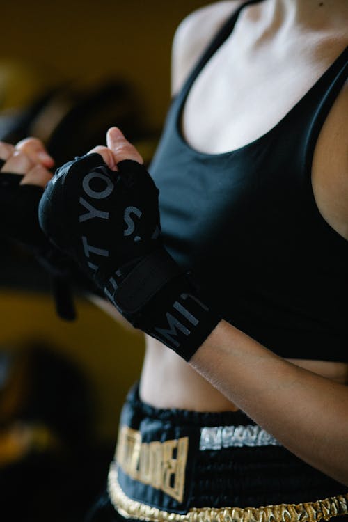 Crop unrecognizable female athlete in black sportswear raising bandaged hands on blurred background