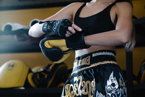 Free Faceless crop sportswoman in dark sportswear fastening boxing glove on hand while preparing for training Stock Photo