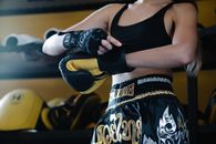 Faceless crop sportswoman in dark sportswear fastening boxing glove on hand while preparing for training