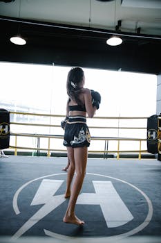 Full-length view of a female boxer training inside a gym ring, showcasing strength and determination.