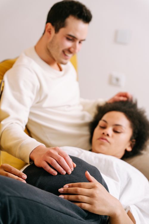 Free Happy couple enjoying an intimate moment during pregnancy, with hands on belly inside a cozy room. Stock Photo