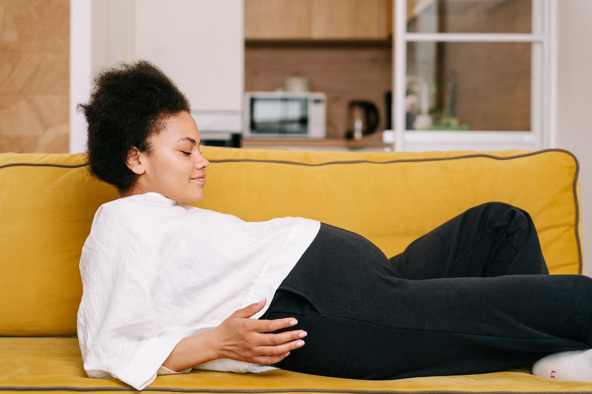 Gravid kvinna som vilar avslappnat på en soffa med benen upp