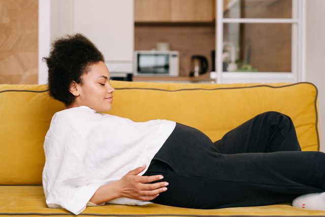 Femme enceinte détendue sur un canapé, la main posée sur son ventre