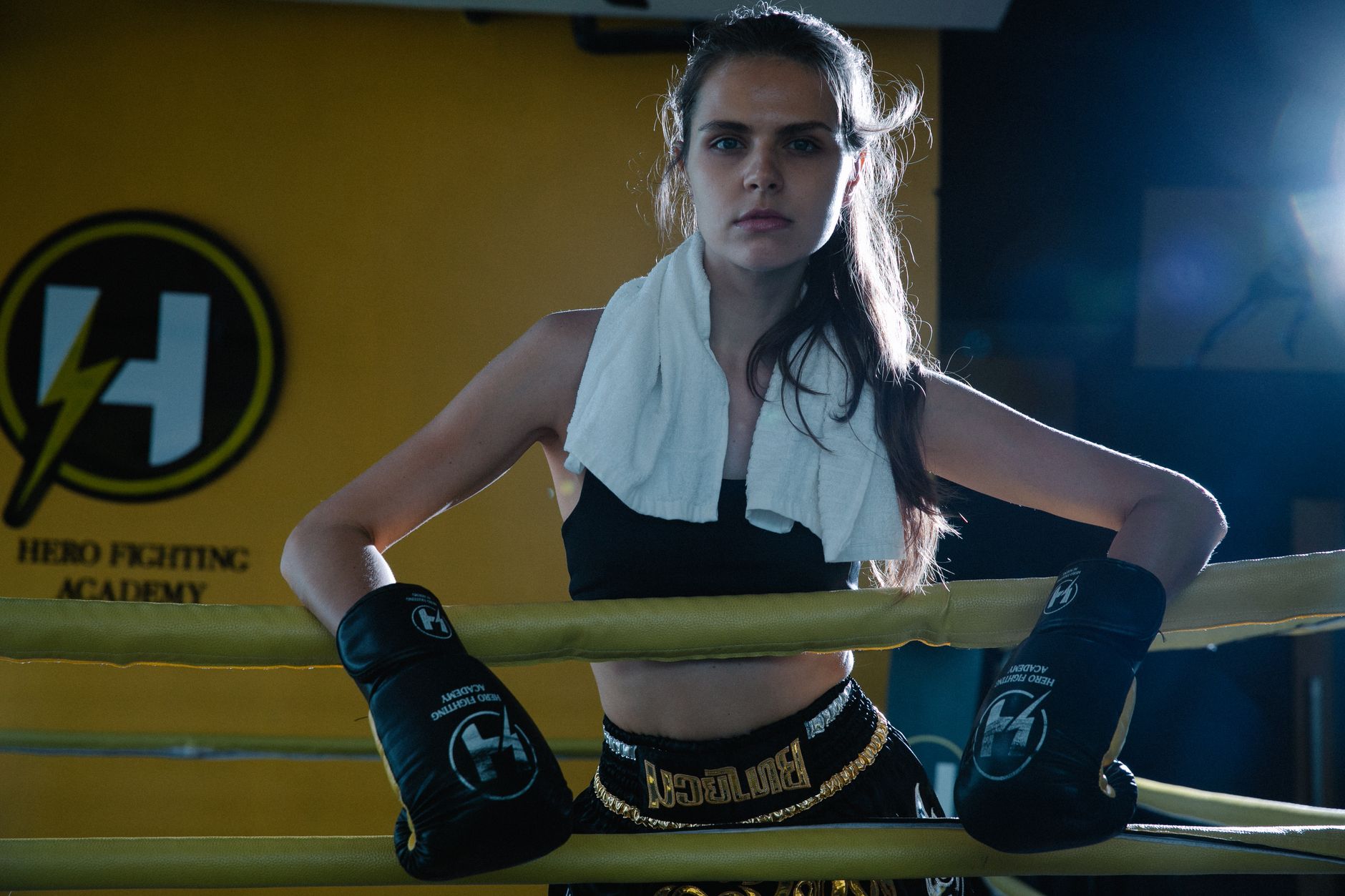 Female boxer stands confidently in ring with gloves and towel.
