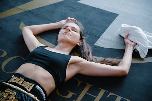 A Woman in Black Crop Top Holding a Towel Lying on the Floor