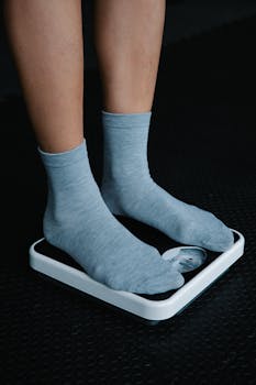 Close-up of feet in gray socks on a weighing scale on a dark floor.