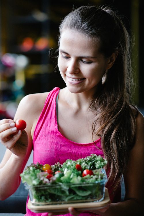 Free Smiling woman in pink tank top holding a fresh green salad with cherry tomatoes. Stock Photo