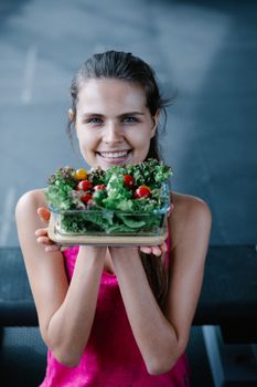 Healthy lifestyle portrait of a smiling woman holding a fresh salad bowl indoors.