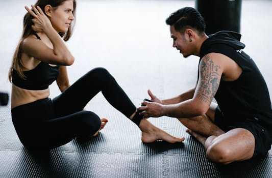 A man helps a woman wrap her hands before a martial arts workout in a gym setting.