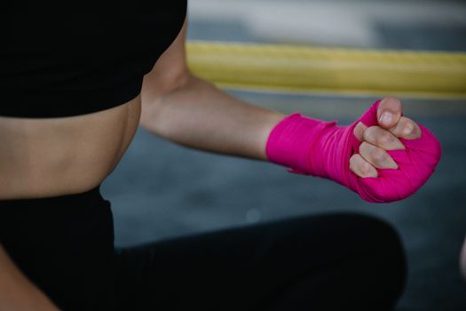 Female boxer with pink wraps preparing for training, showing strength and determination.