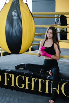 Confident woman wraps hands with pink bandages in a modern gym setting, boxing in focus.