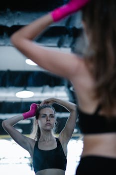 Focused woman adjusting pink bandages in gym mirror, preparing for workout.