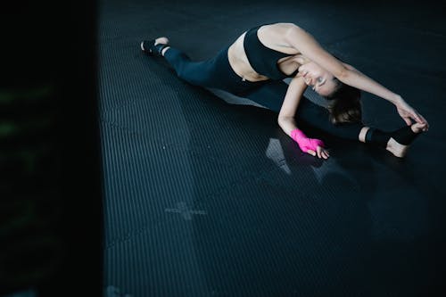 Free Woman in Black Tank Top and Leggings Doing Stretching on Black Puzzle Mat Stock Photo