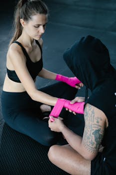 A man and woman prepare for training by wrapping hands with pink bandages indoors.