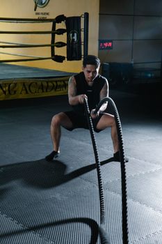 Man working out with battle ropes in a gym for strength and fitness.
