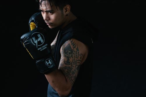 Free Portrait of a determined boxer in dark studio setting, showcasing tattoos and boxing stance. Stock Photo
