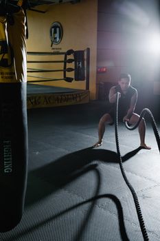 A man engages in an intense battle ropes workout in a gym setting.