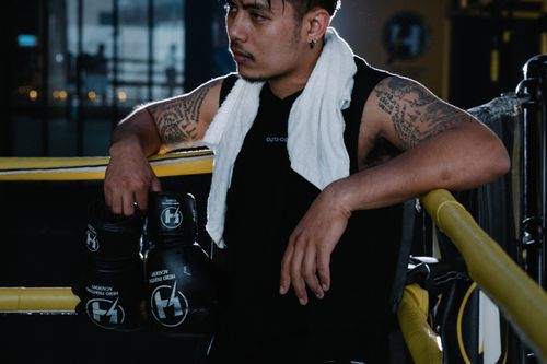 Free Athlete with tattoos resting in a boxing ring, wearing sports clothing with gloves. Stock Photo